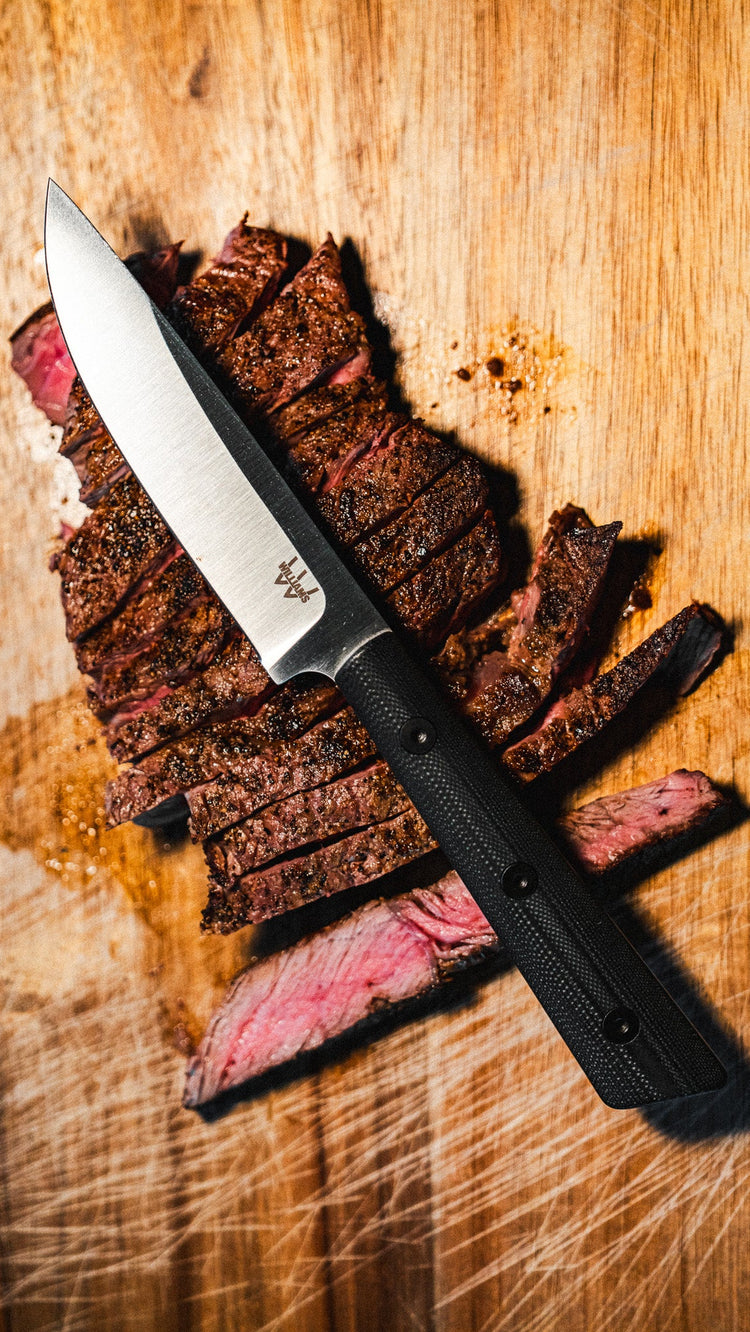 Knife with black handle on sliced steak on a wooden cutting board