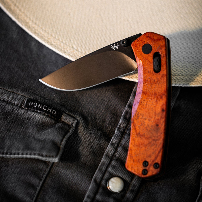 Folding knife with wooden handle on a person wearing a hat and dark shirt